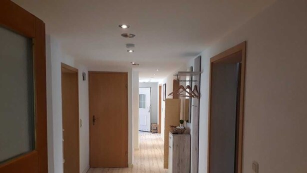 Un couloir avec un plancher en bois, un réfrigérateur et un porte-manteau mural.