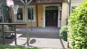 Un panier de basket, un banc en bois, une porte et un petit buisson.