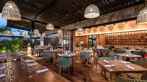A restaurant with wooden tables and chairs, hanging pendant lights, and a brick wall with shelves. - Las Brisas Merida (Mérida)