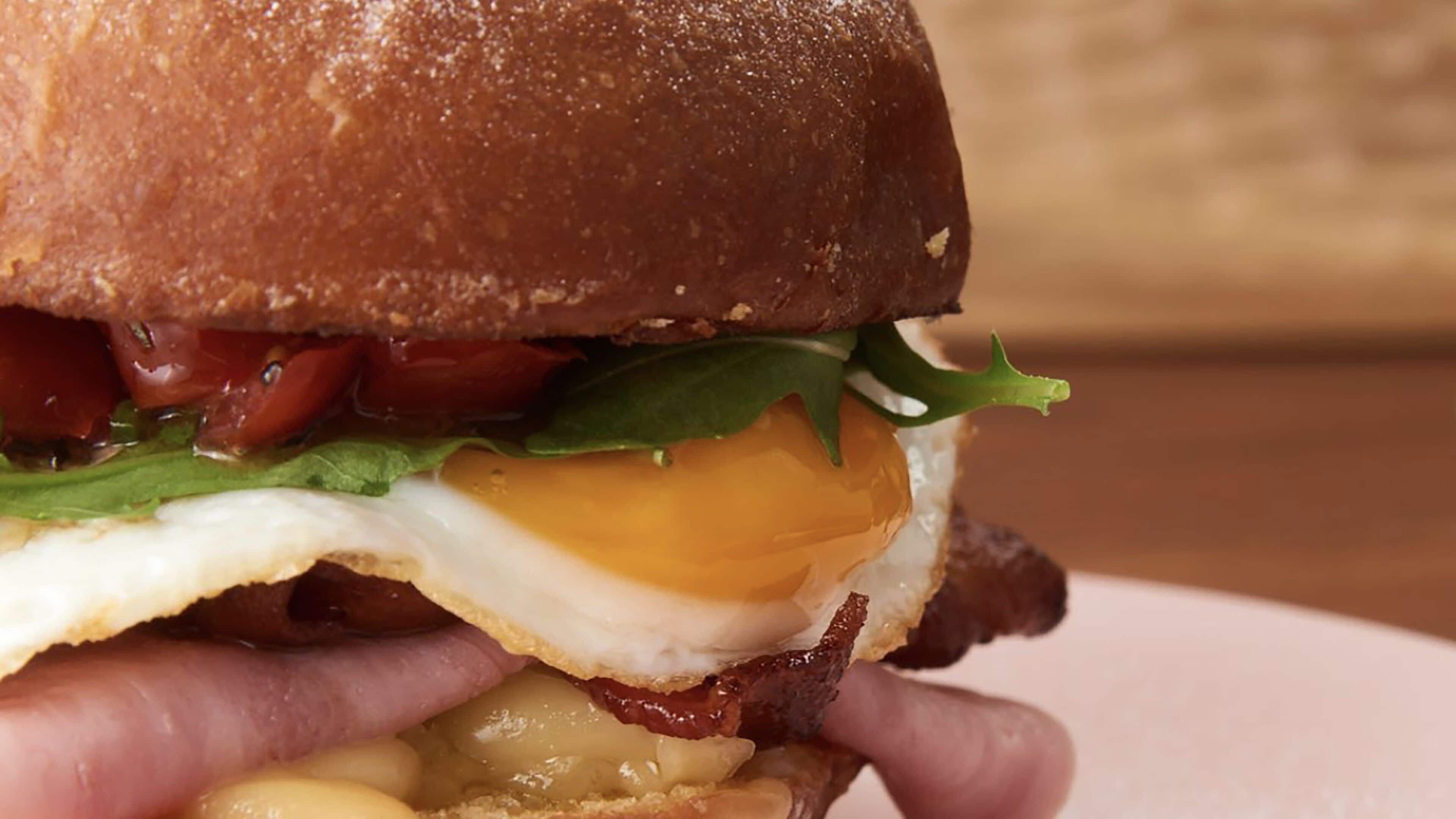 A close-up of a sandwich with visible ingredients like lettuce, tomato, egg, cheese, and bacon.