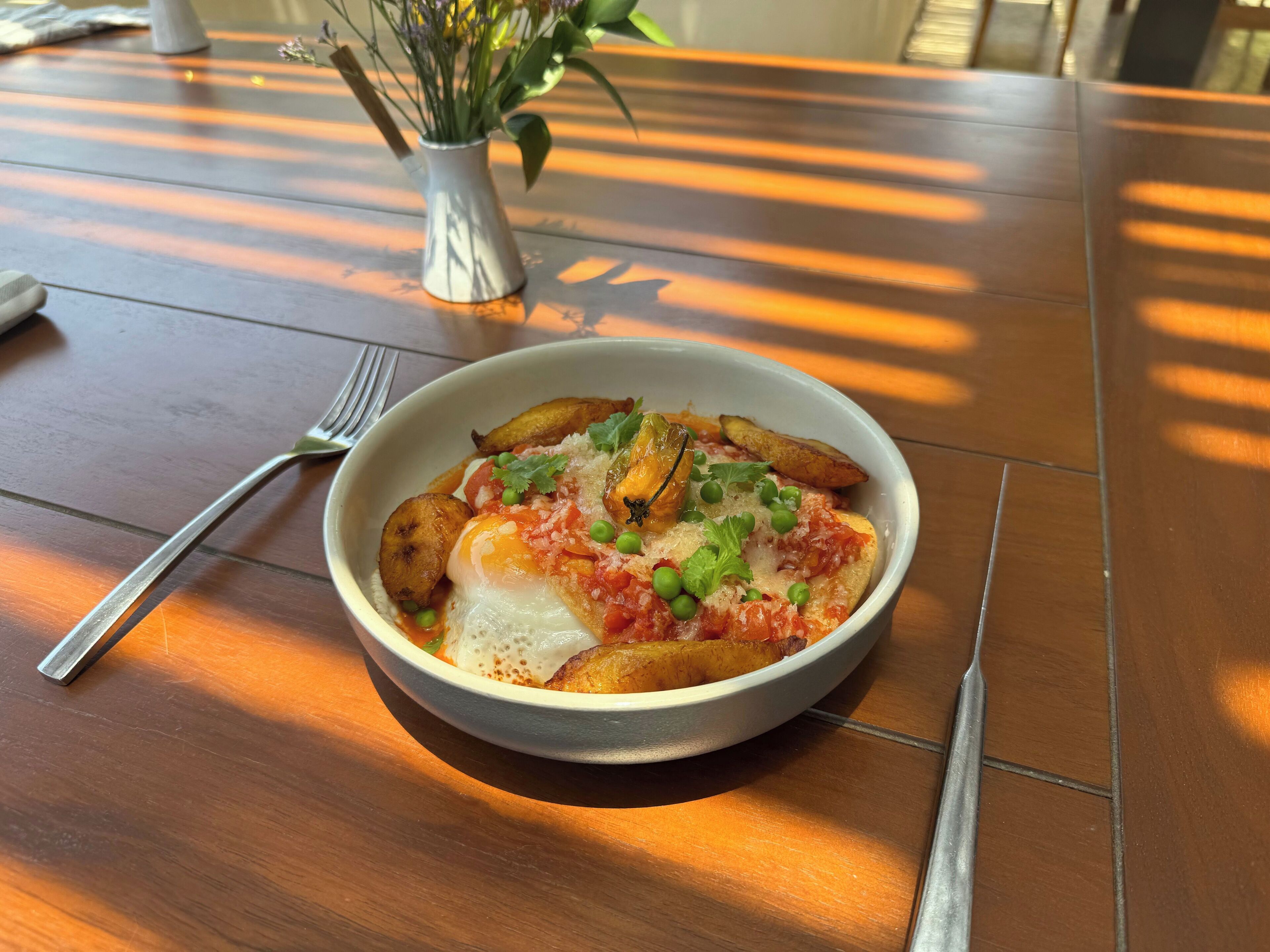 A bowl of food on a wooden table with a fork and knife beside it.