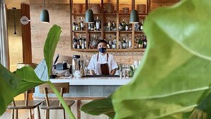 A bar area with a bartender, shelves of liquor bottles, and hanging lights. - Las Brisas Merida (Mérida)