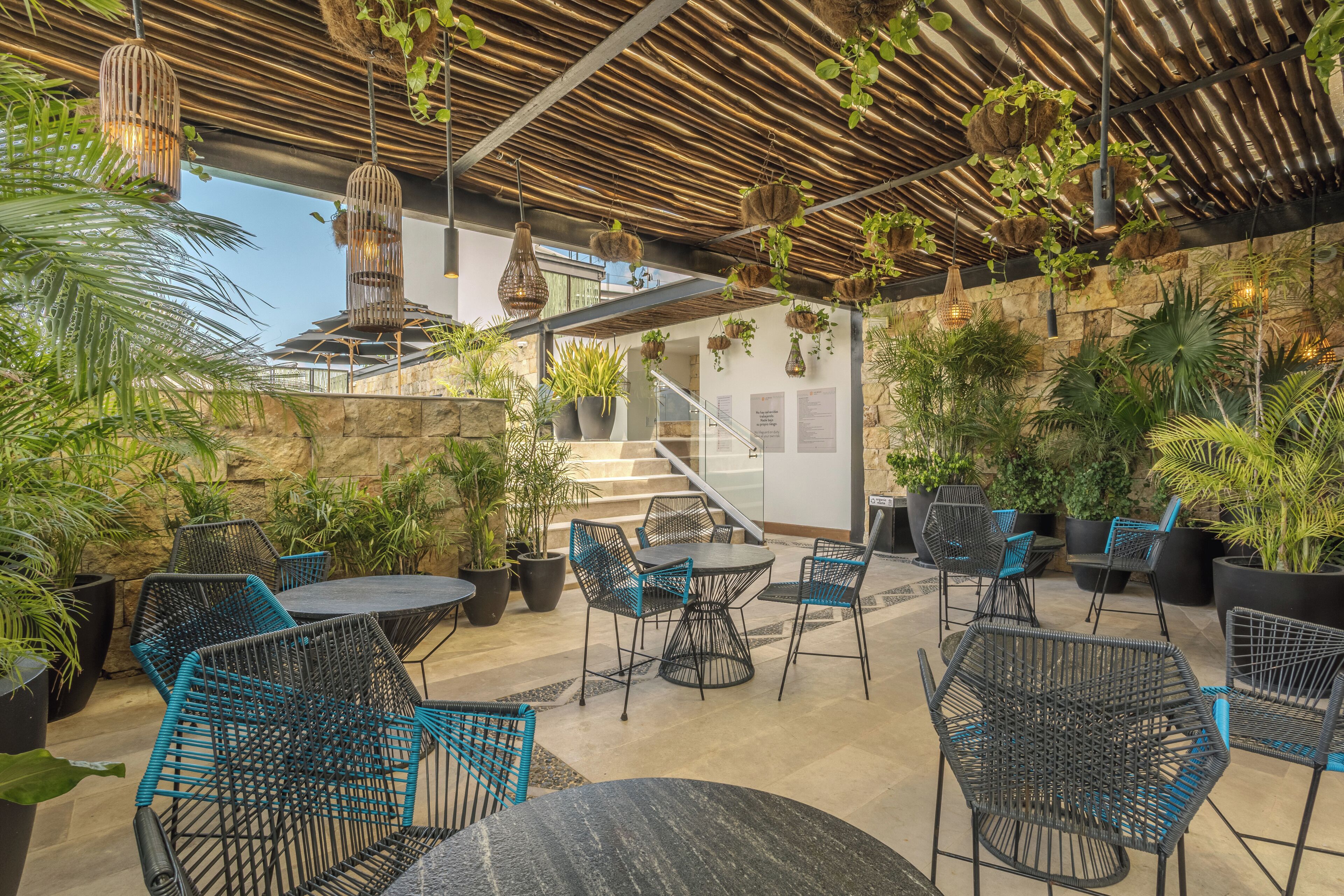 An outdoor patio area with round tables and chairs, surrounded by potted plants and hanging planters.