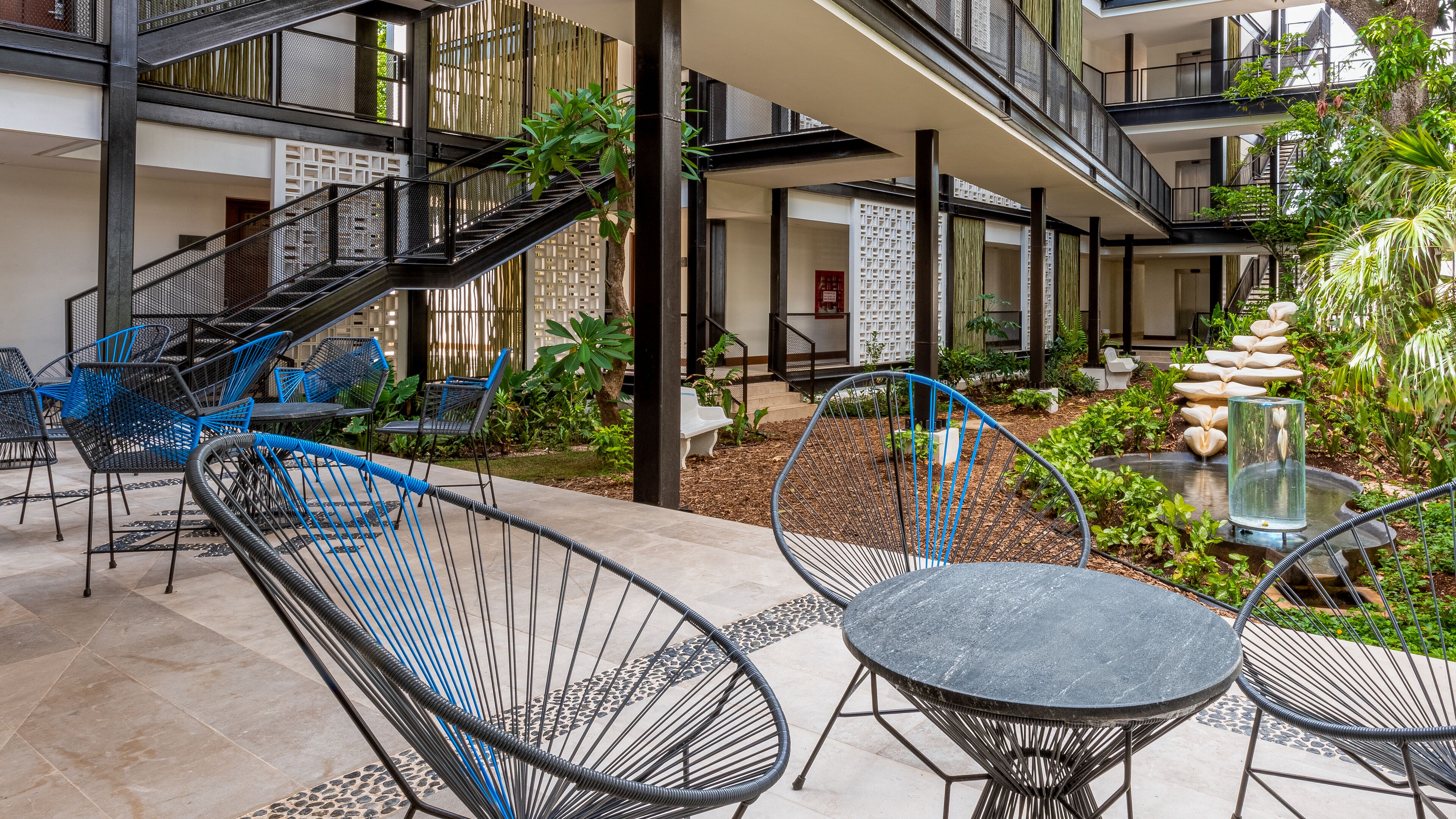 Una terraza al aire libre con varios niveles, zonas de estar, una escalera y un pequeño jardín con plantas y una fuente de agua.