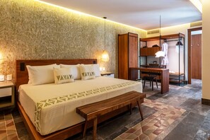 Una habitación de hotel con una cama grande, un banco de madera, un escritorio con una silla y un armario.