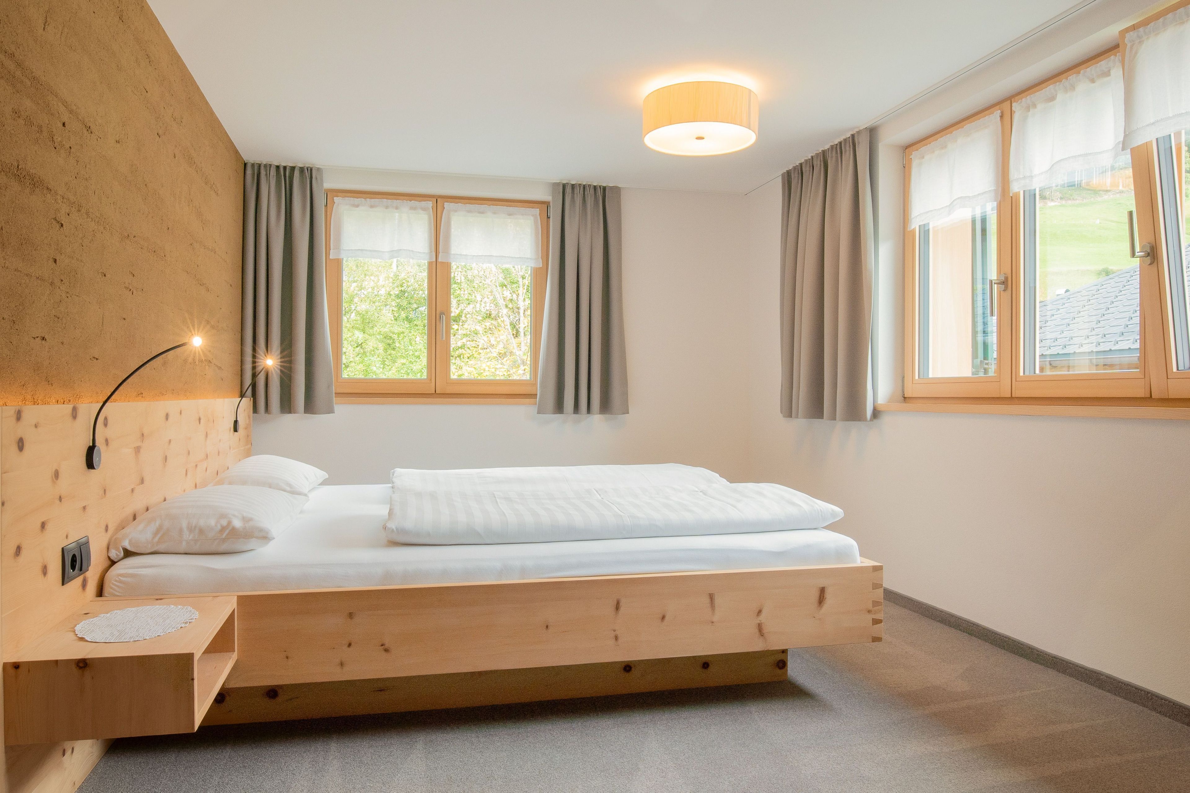 A modern bedroom with a wooden bed, a bedside table, a lamp, and a window with curtains.