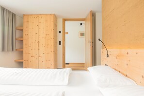 A bedroom with two beds, a wooden wardrobe, a door leading to another room, and a wall-mounted light fixture. - Vacation apartment Gutgehen (1-2 persons) - Moosbrugger Rosmarie - Haus WohlSEIN (Schoppernau)