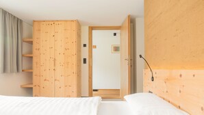 A bedroom with two beds, a wooden wardrobe, a door leading to another room, and a wall-mounted light fixture. - Vacation apartment Gutgehen (1-2 persons) - Moosbrugger Rosmarie - Haus WohlSEIN (Schoppernau)