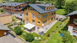A multi-story building with balconies, a patio area, and a view of a green landscape. - Vacation apartment Gutgehen (1-2 persons) - Moosbrugger Rosmarie - Haus WohlSEIN (Schoppernau)