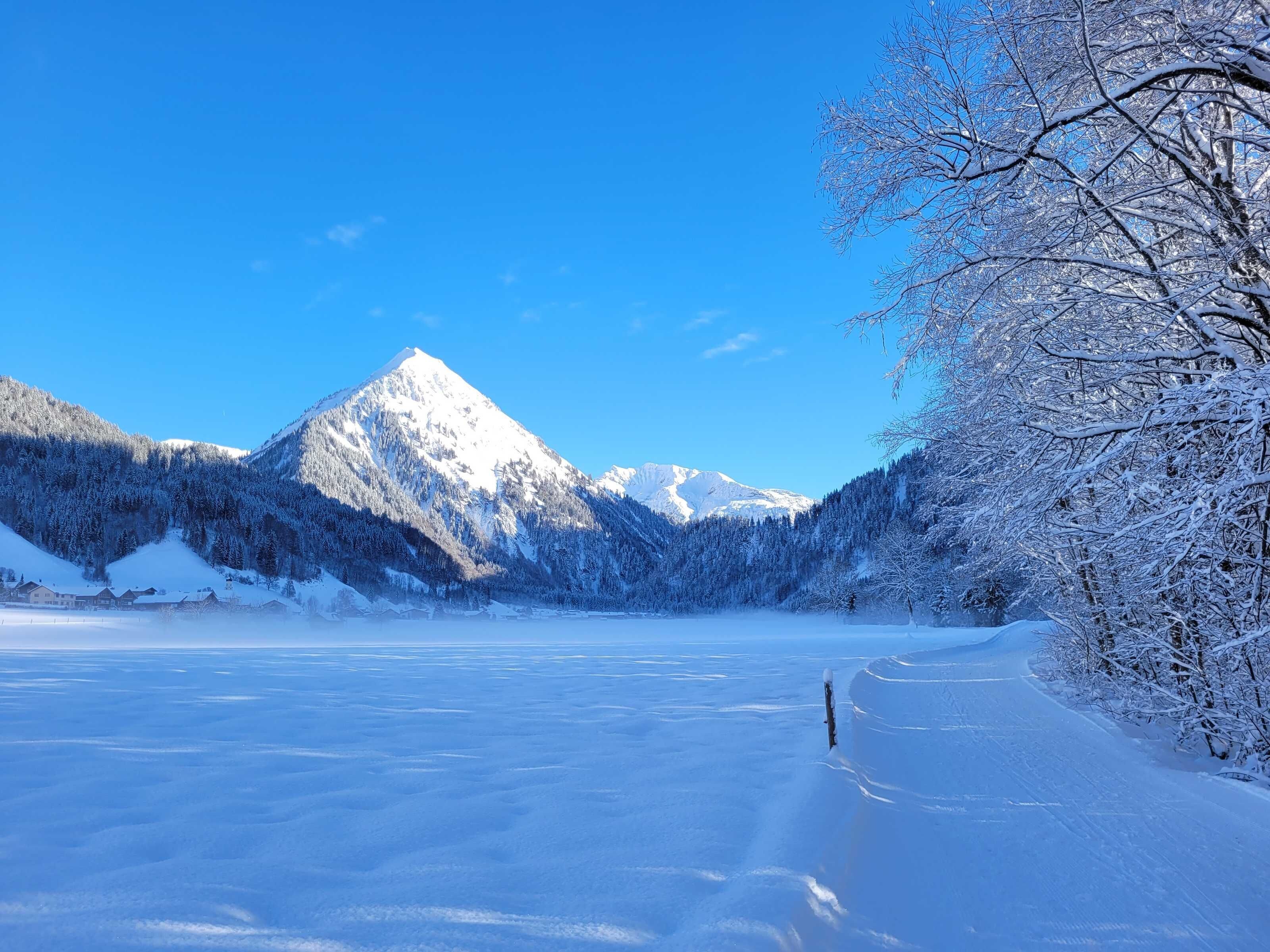 Paisagem coberta de neve com montanha, lago congelado e um caminho.