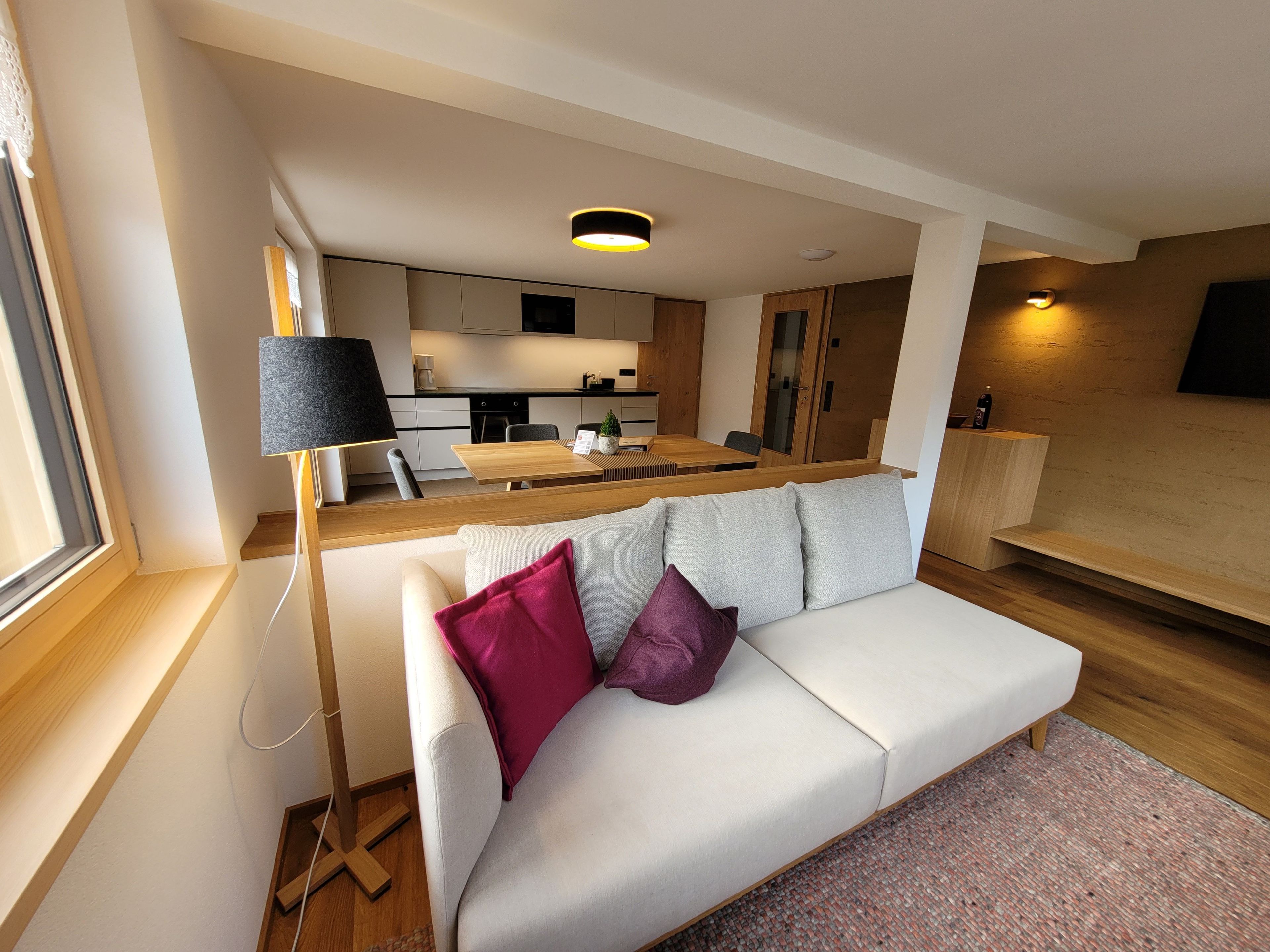A modern living room with a sofa, a coffee table, and a dining area with a kitchen in the background.