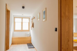 Un pasillo con un banco de madera, una ventana y ganchos en la pared.