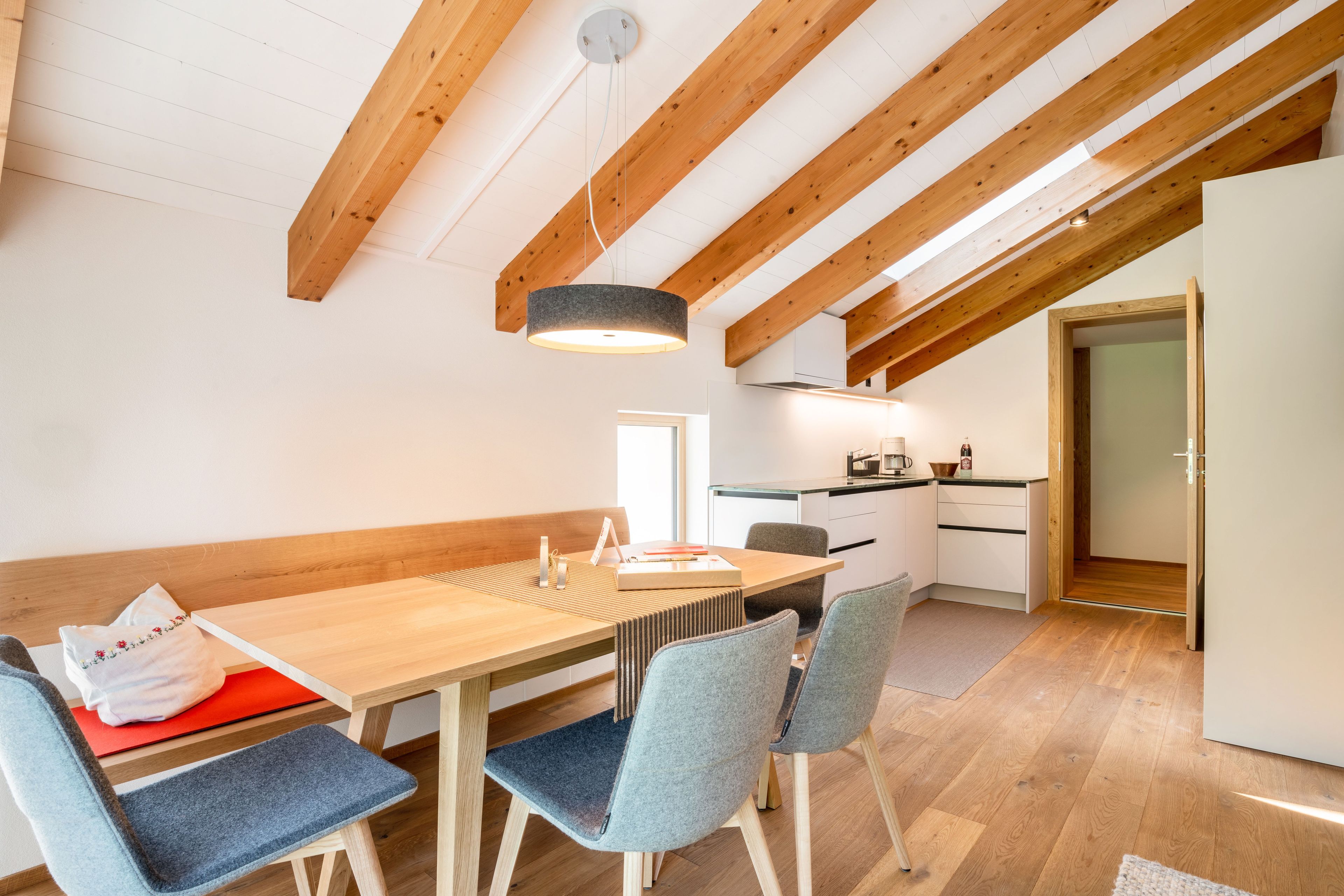 A dining area with a wooden table, grey upholstered chairs, and a ceiling with exposed wooden beams.