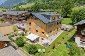 A multi-story building with balconies, a patio area, and a view of a green landscape. - Vacation apartment Enjoy (2-4 persons) - Moosbrugger Rosmarie - Haus WohlSEIN (Schoppernau)
