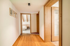 Un couloir doté d’un plancher en bois, une porte visible donnant sur une salle de bain et des tableaux encadrés accrochés au mur.