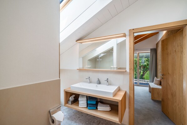 A modern bathroom with a large mirror, a white sink, and a wooden vanity.