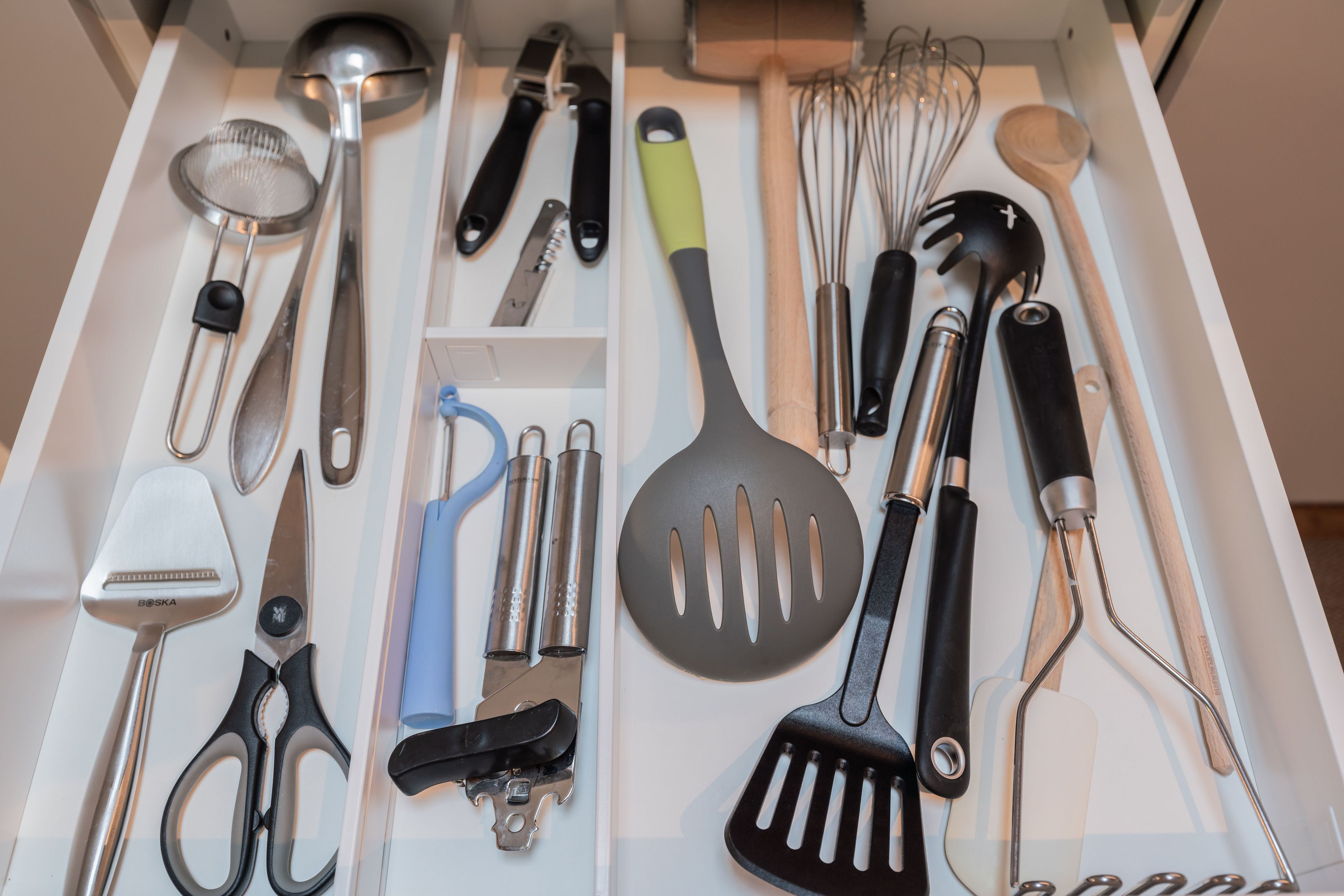 A drawer containing various kitchen utensils including a spatula, whisk, and scissors.