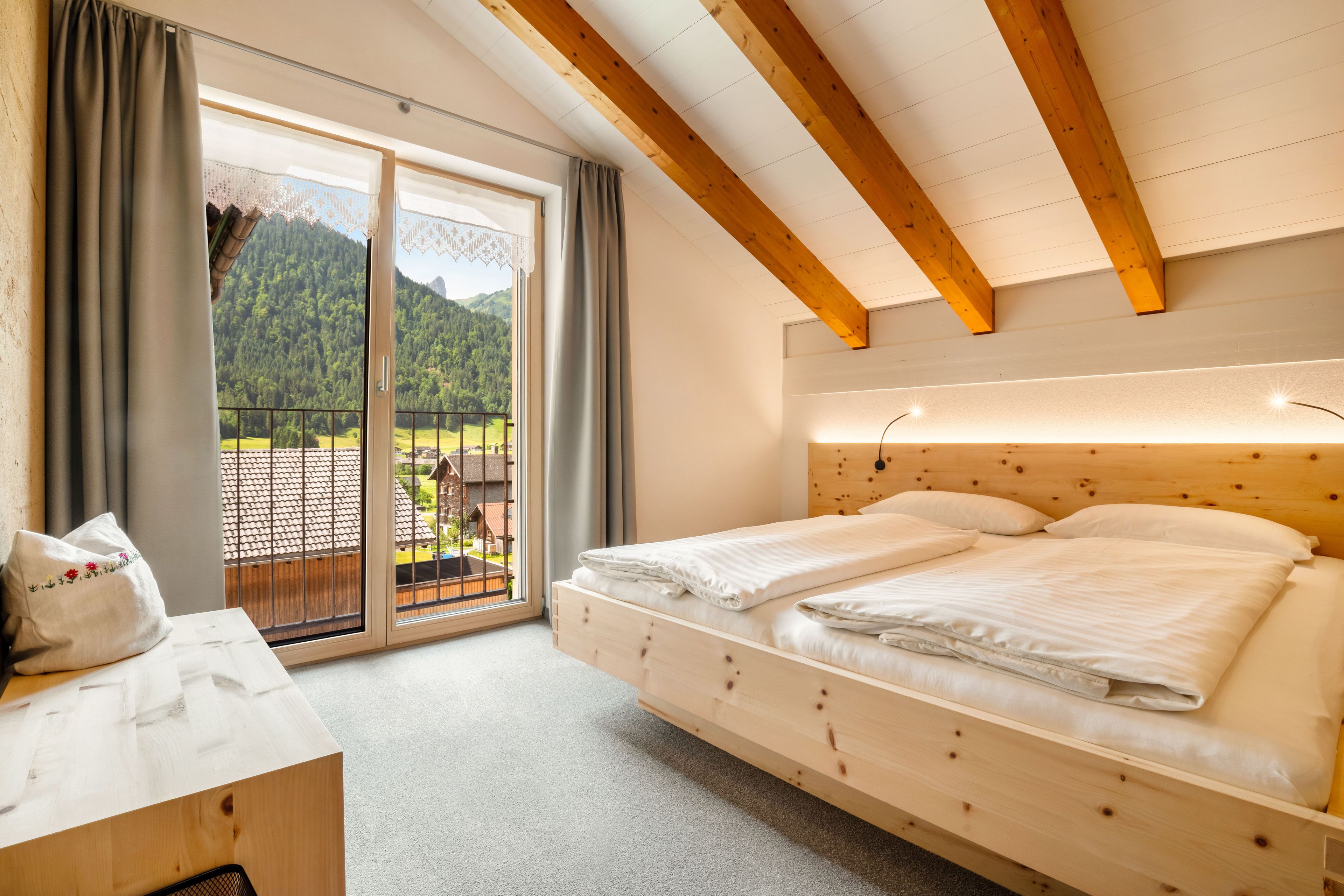 A room with a wooden bed, a desk, and a view of a mountain through a sliding door.