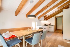 A dining area with a wooden table, grey upholstered chairs, and a ceiling with exposed wooden beams.