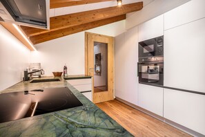 A modern kitchen with a built-in stove, a wooden door, and white cabinetry. - Vacation apartment Enjoy (2-4 persons) - Moosbrugger Rosmarie - Haus WohlSEIN (Schoppernau)