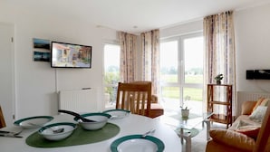 Un comedor con una mesa redonda dispuesta para cuatro personas, un televisor montado en la pared y vistas al exterior a través de amplios ventanales.