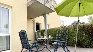 Un patio al aire libre con dos sillas y una mesa, una sombrilla verde y un edificio con balcón.