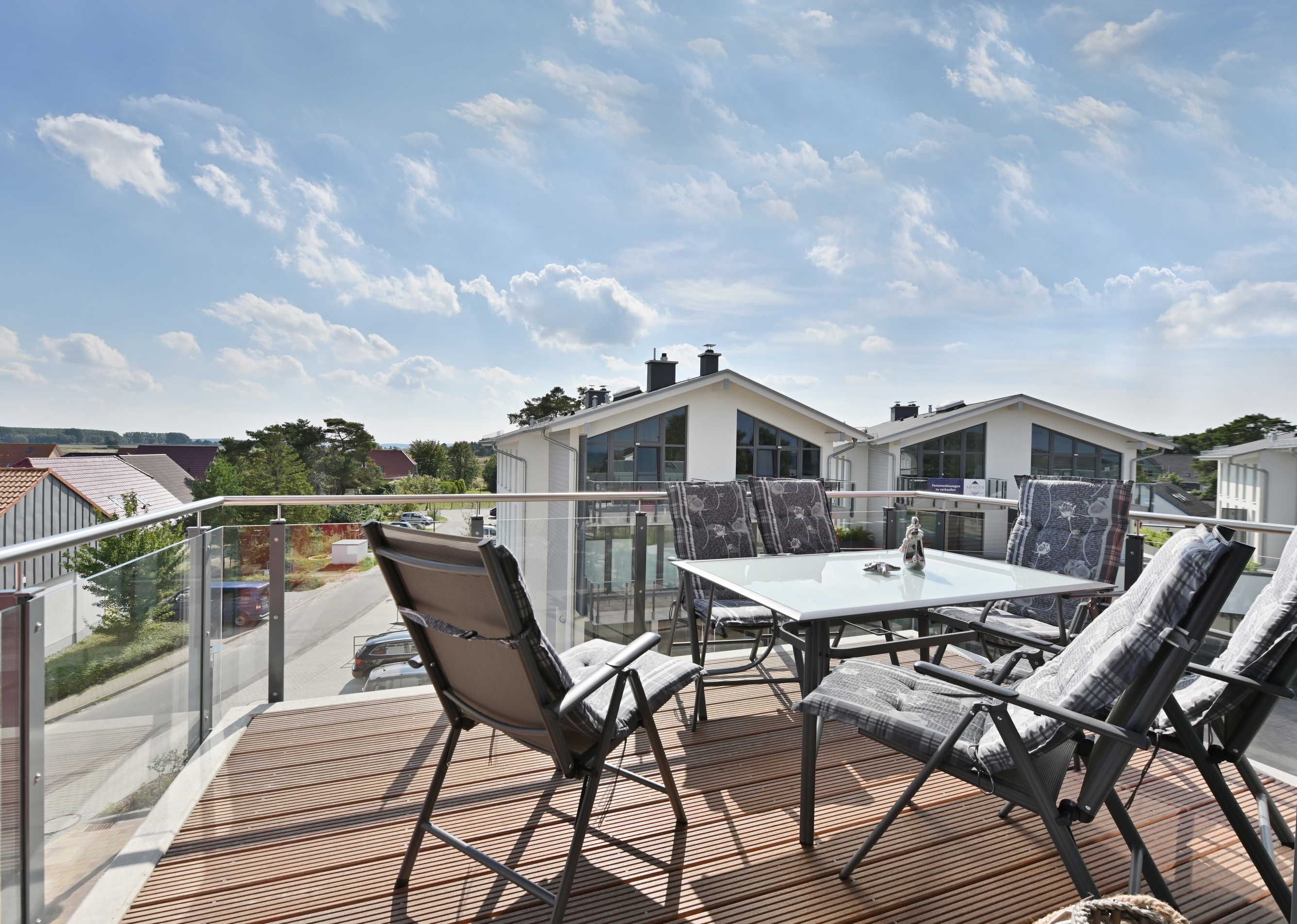 En balkon med et bord og stole, der kigger ud over et boligområde med moderne huse.