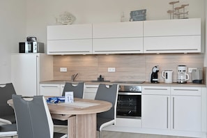 Eine moderne Küche mit weißen Schränken, einem eingebauten Backofen und einem Essbereich mit rundem Tisch und Stühlen.