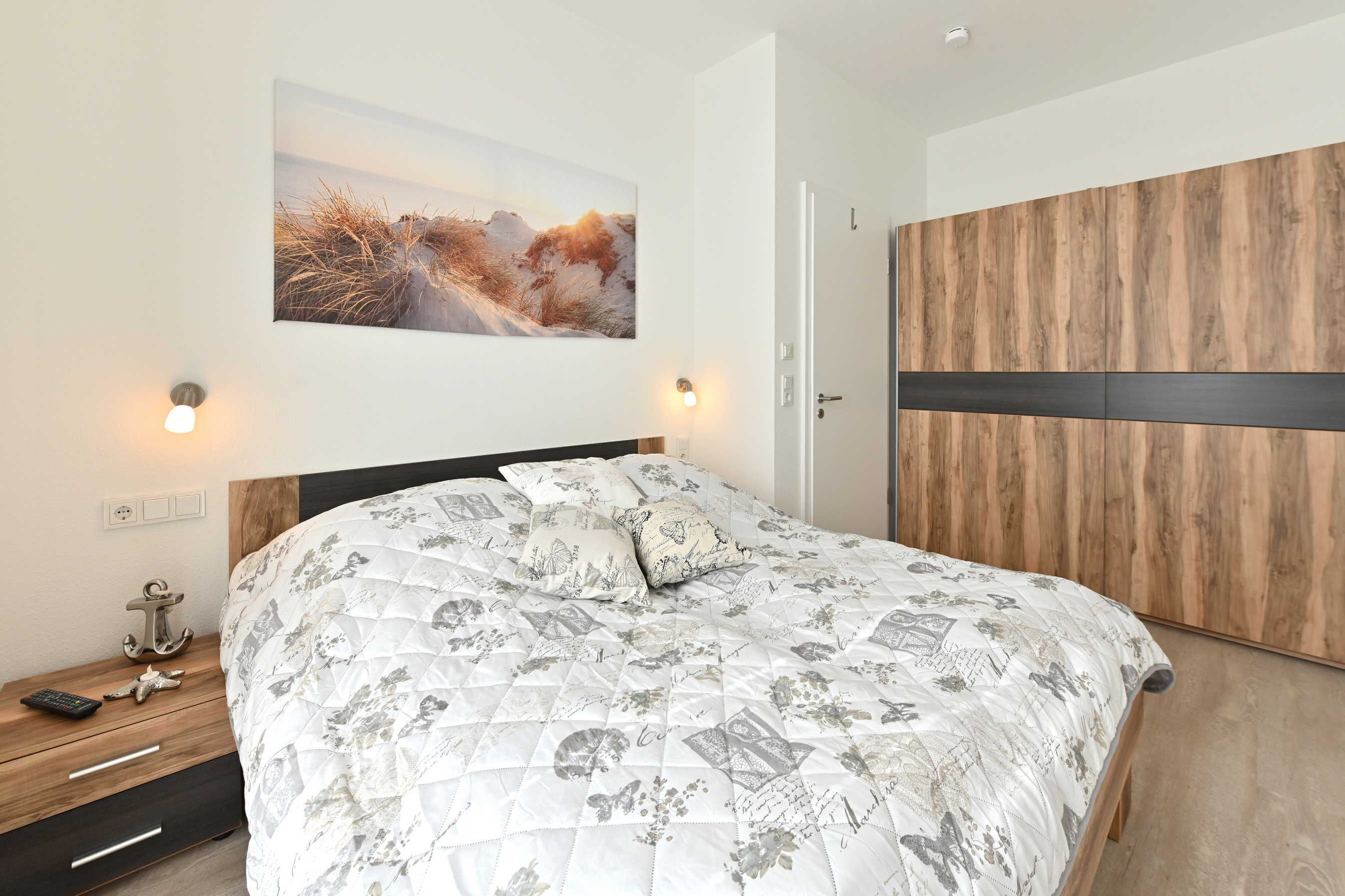 A bedroom with a bed, a nightstand, a wall-mounted picture, and a wardrobe.