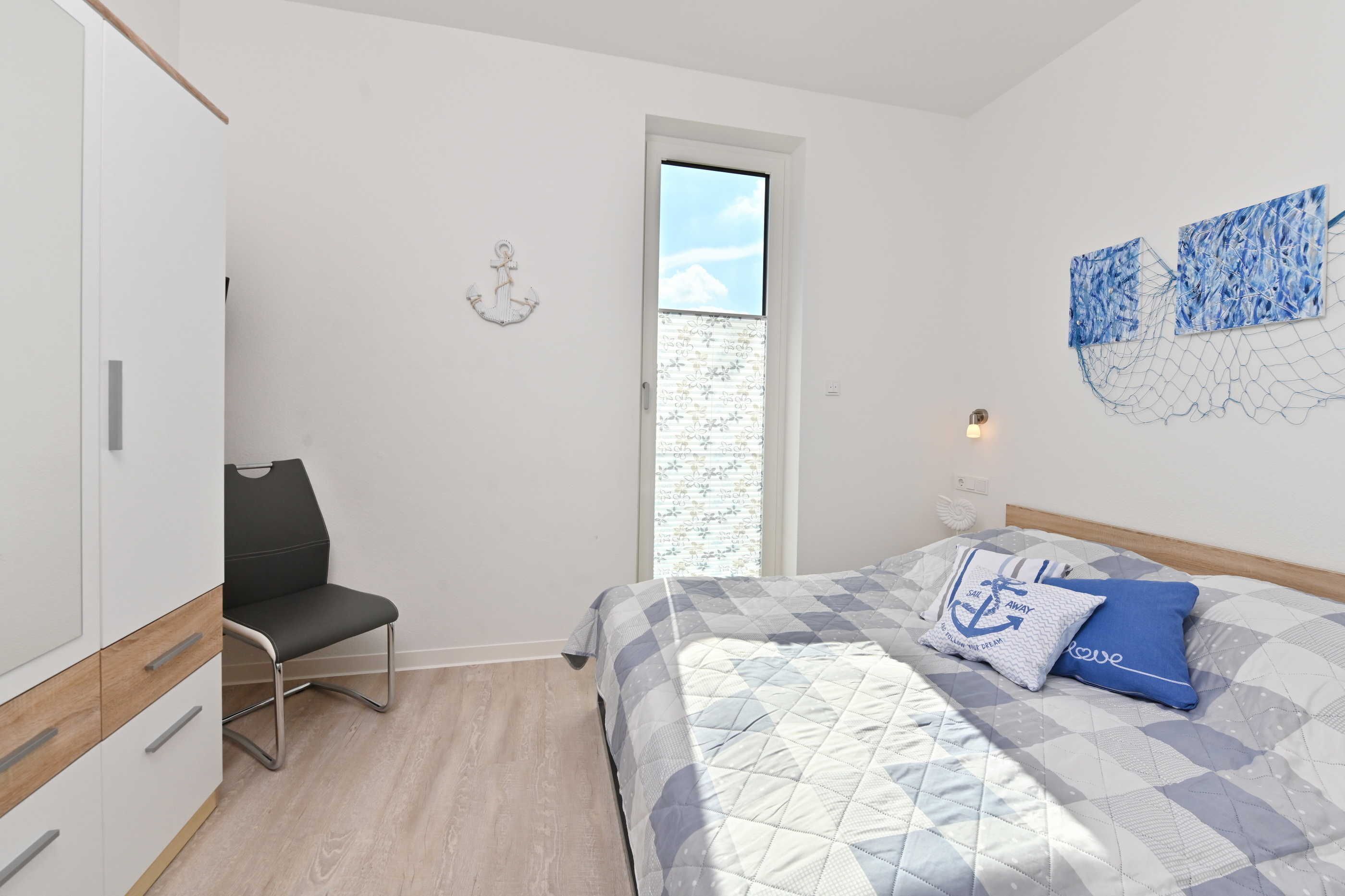 A bedroom with a bed, a chair, a wardrobe, and a window.