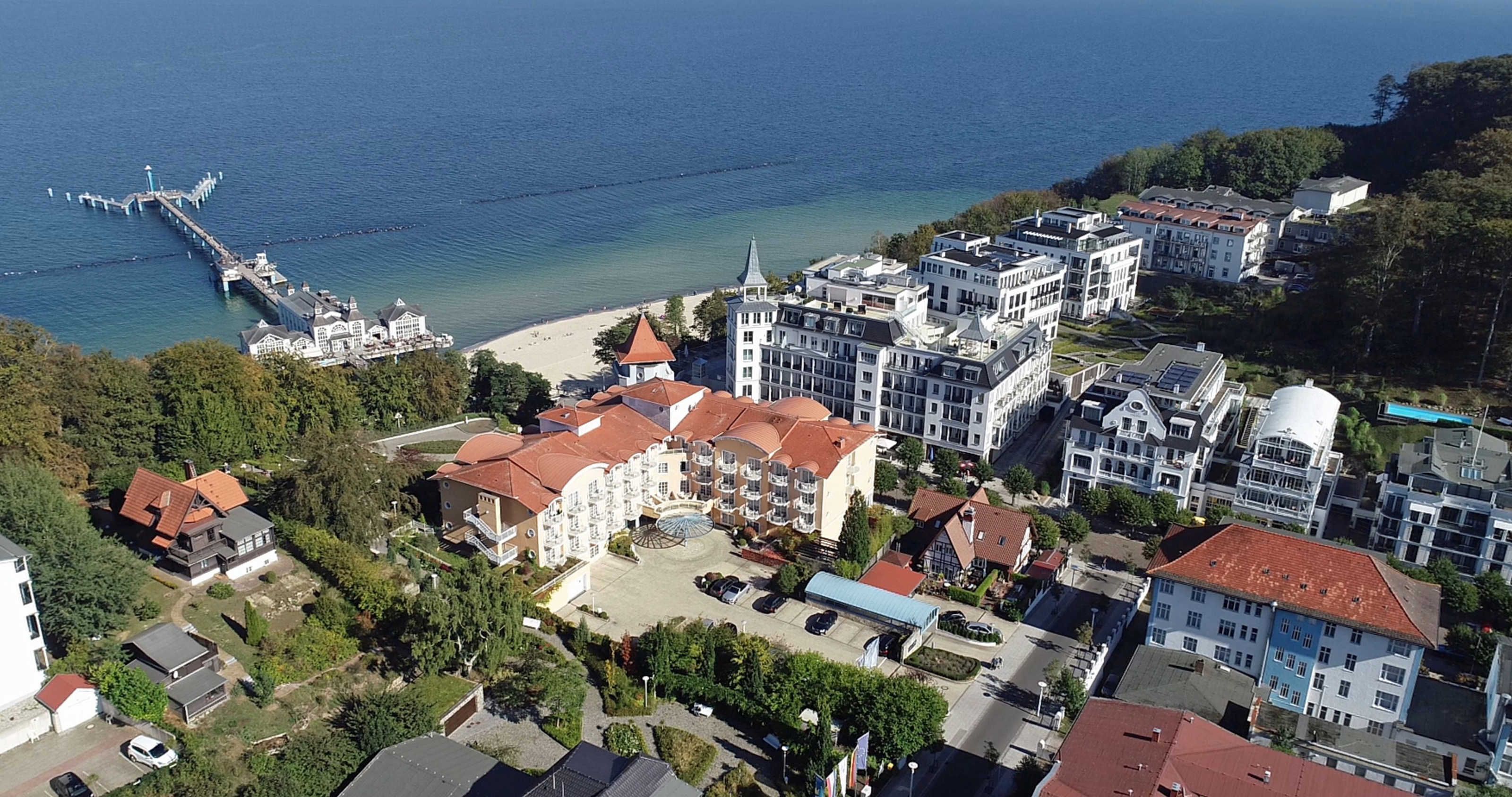 An aerial view of a coastal town with a pier extending into the sea, surrounded by residential buildings and a beach.