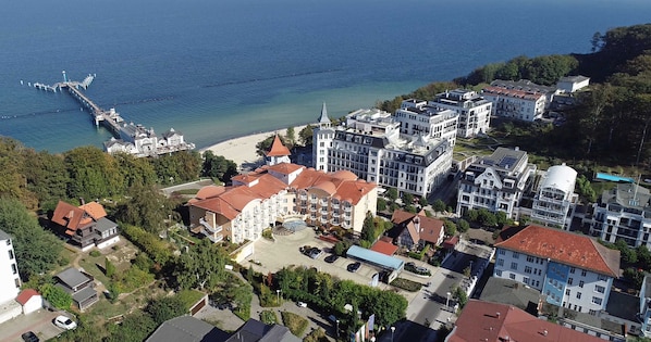 An aerial view of a coastal town with a pier extending into the sea, surrounded by residential buildings and a beach.