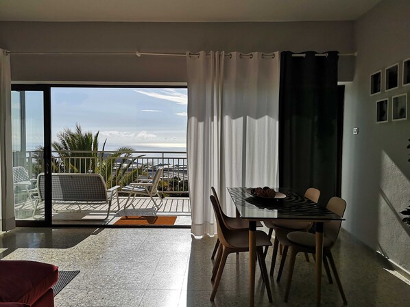 A dining area with a table and chairs, a view of the sea, and a balcony with outdoor furniture.