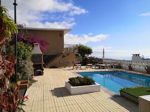 A rooftop pool area with a barbecue, outdoor seating, and a view of the sea.