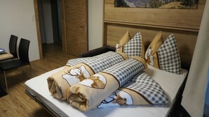 A bedroom with a bed, checkered pillows, a mountain view painting, and a wooden door. - Alblerhof - Apartment (2-5 people) (Pfunds)