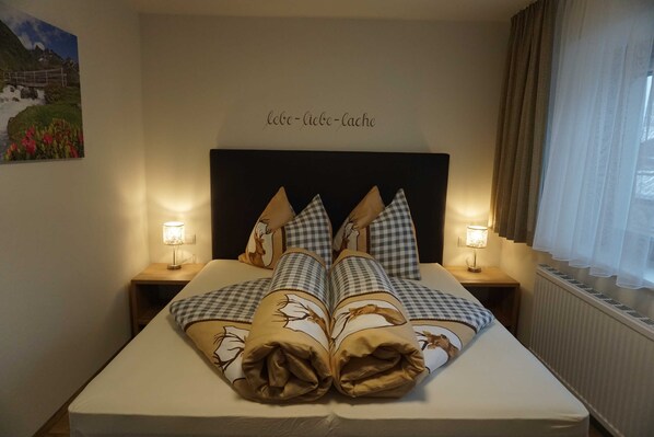 A neatly made bed with checkered pillows, two bedside lamps, a wall-mounted picture, and a sign with text. - Alblerhof - Apartment (2-5 people) (Pfunds)