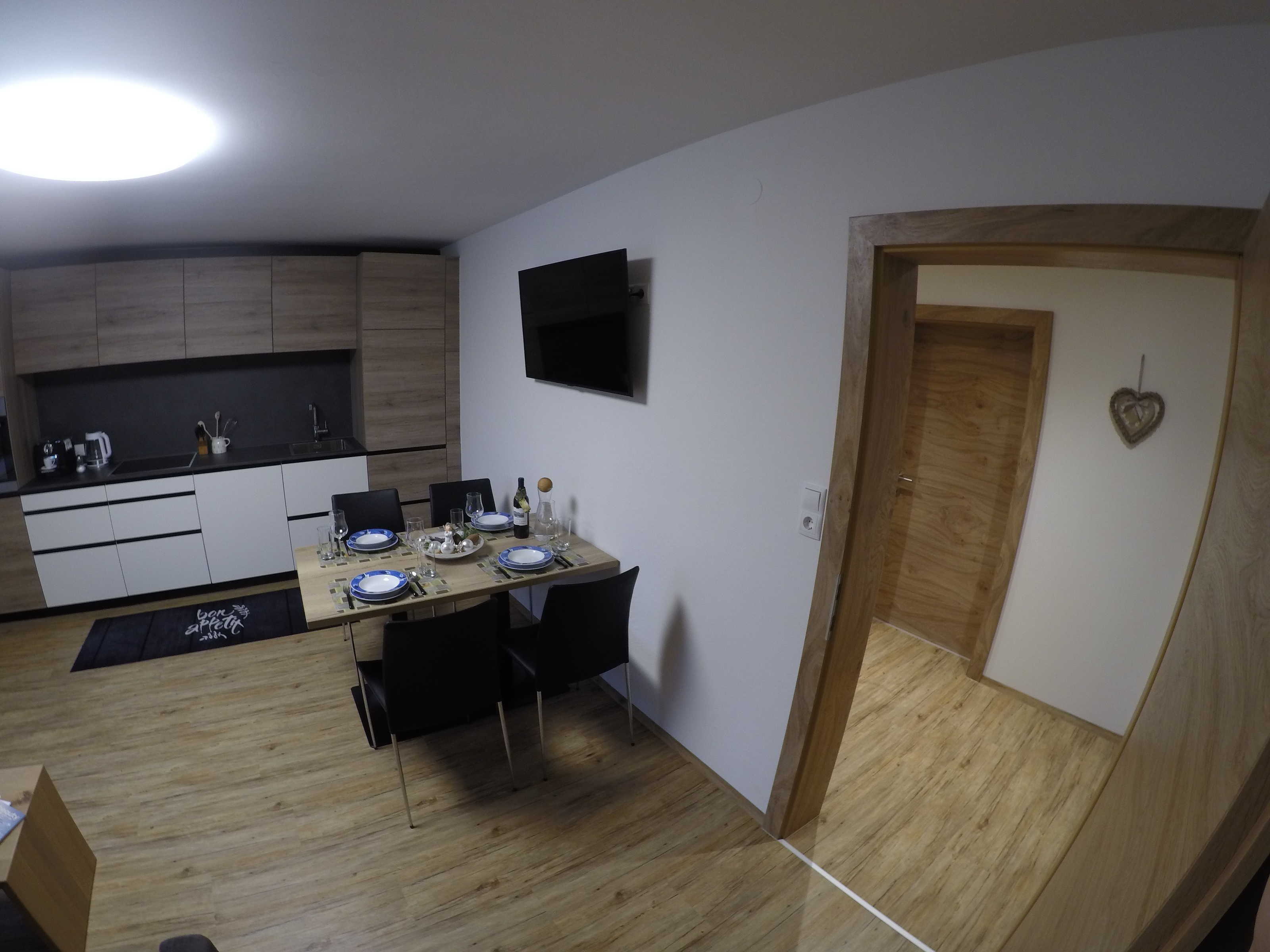 A compact kitchen with a dining area, a flat-screen TV, and a wooden door with a heart-shaped decoration.