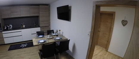 A compact kitchen with a dining area, a flat-screen TV, and a wooden door with a heart-shaped decoration.