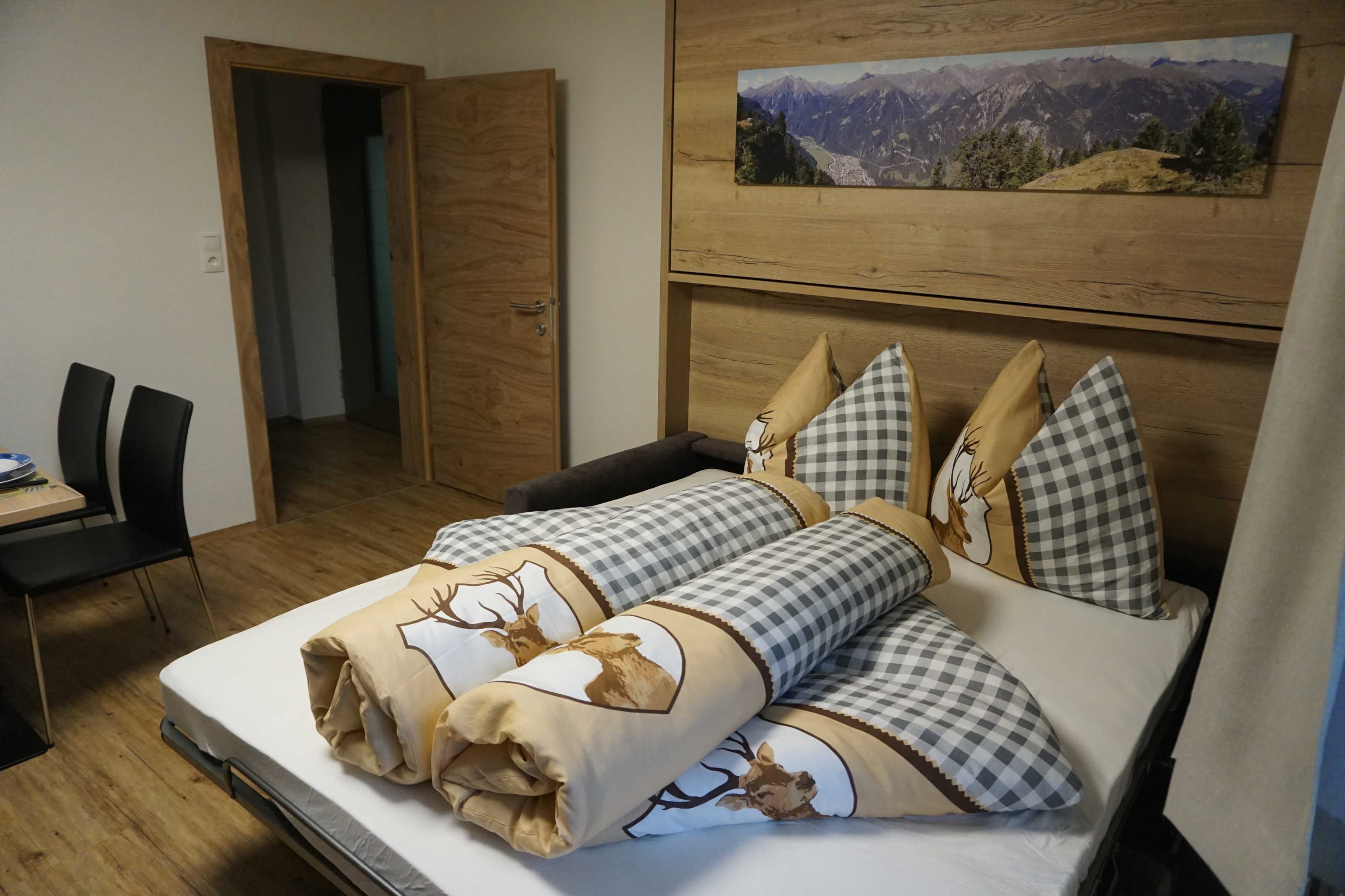 Een slaapkamer met een bed, geruit bedkussen, een schilderij van een uitzicht op de bergen en een houten deur.