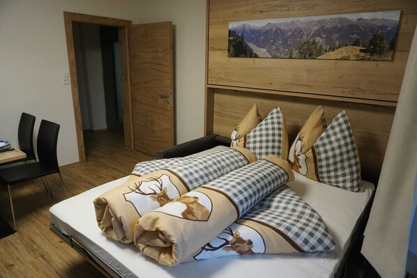 A bedroom with a bed, checkered pillows, a mountain view painting, and a wooden door.