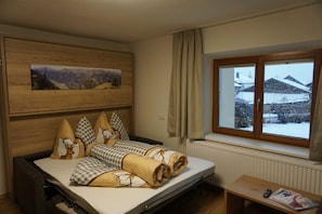 Una habitación con una cama, una ventana que ofrece vistas a edificios cubiertos de nieve, un cabecero de madera y un cuadro en la pared.