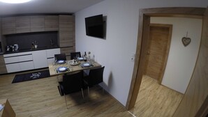 A compact kitchen with a dining area, a flat-screen TV, and a wooden door with a heart-shaped decoration. - Alblerhof - Apartment (2-5 people) (Pfunds)