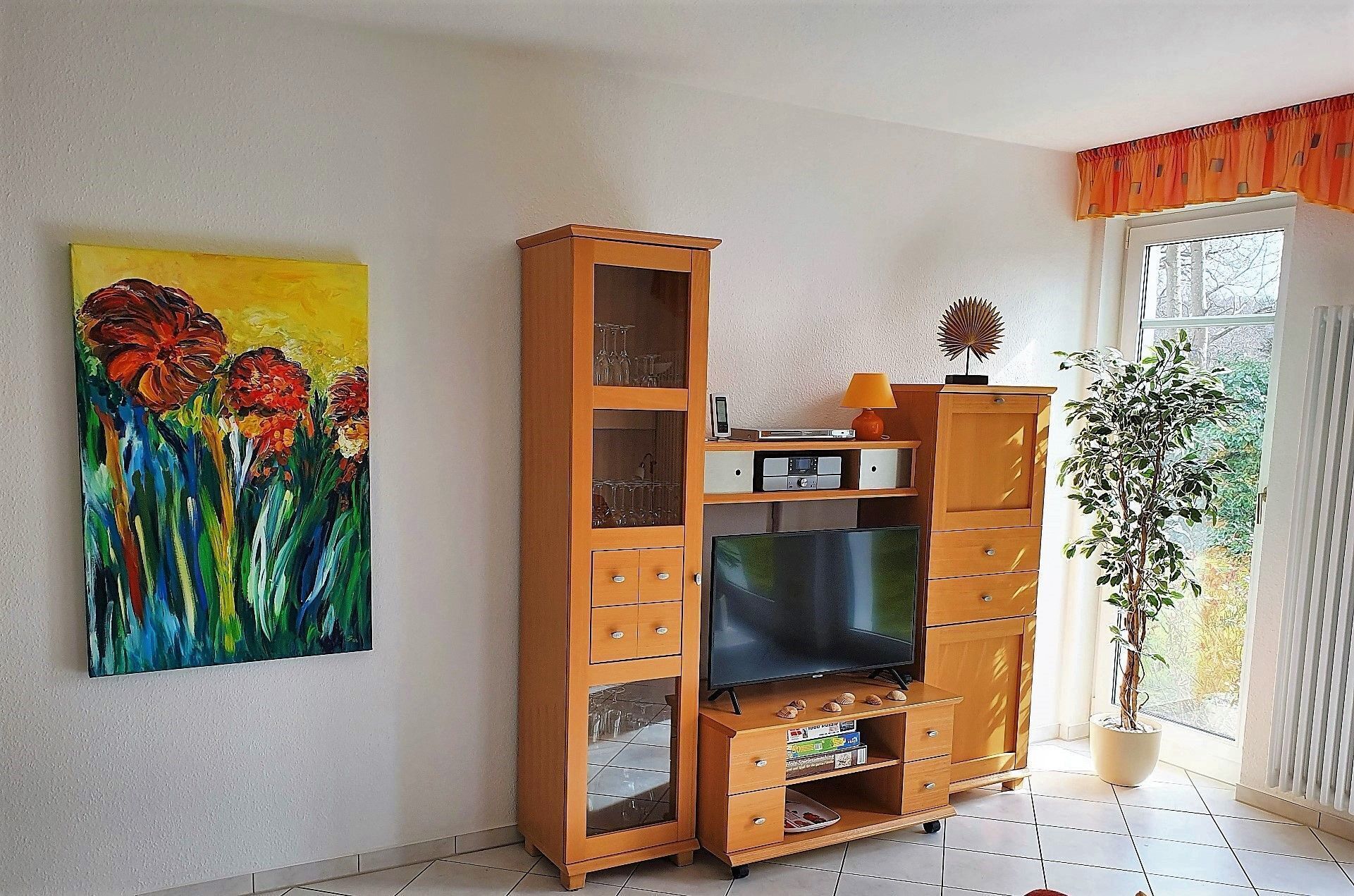 A living room with a wooden entertainment unit, a flat-screen TV, a painting, and a potted plant.