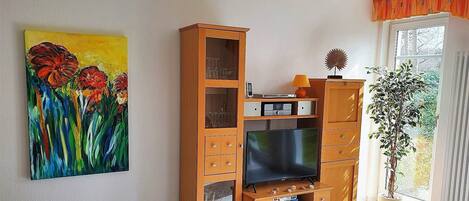 A living room with a wooden entertainment unit, a flat-screen TV, a painting, and a potted plant.