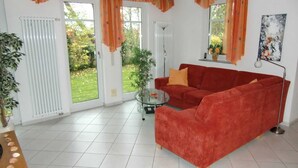 Un salón con sofá rojo, una mesa de centro de cristal y vistas a un jardín a través de amplios ventanales.