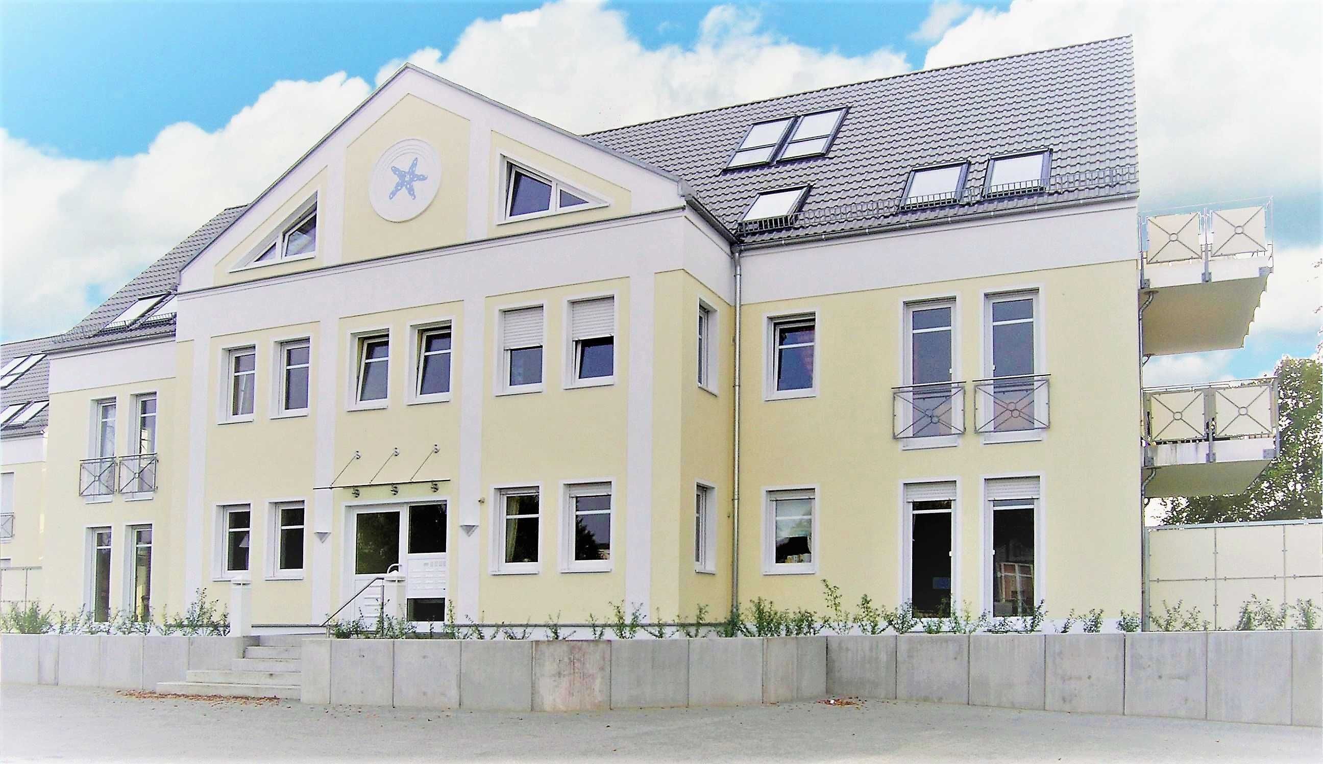Ein mehrstöckiges Gebäude mit gelber Fassade, zahlreichen Fenstern und einem Balkon im zweiten Stock.