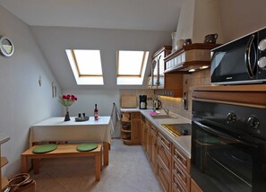 A compact kitchen with skylights, wooden cabinets, a built-in oven, and a dining area with a table and benches.