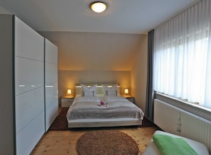 A modern hotel room with a large bed, bedside lamps, a radiator, and a view of the outdoors through sheer curtains.