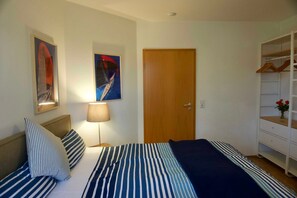 Un dormitorio con cama, mesita de noche, lámpara, puerta de madera y armario con espejo.