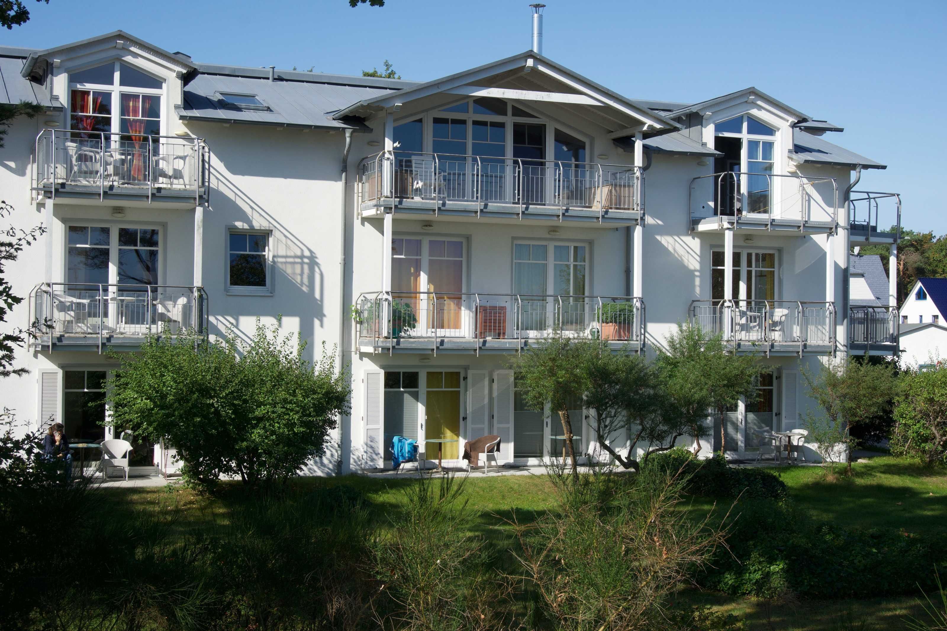 A multi-story residential building with balconies, a covered porch, and a well-maintained lawn.